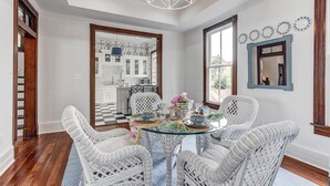 A dining area with wicker chairs, a glass table, and a chandelier. - Home in East End Historic Galveston, Coco Shores (Galveston)