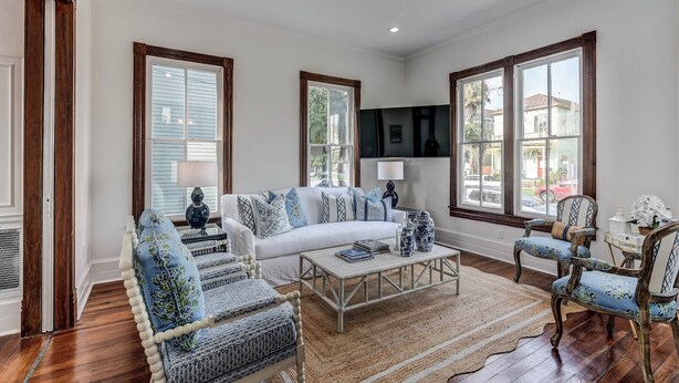 A spacious living room with a white sofa, patterned armchairs, a coffee table, and large windows with wooden frames. - Home in East End Historic Galveston, Coco Shores (Galveston)