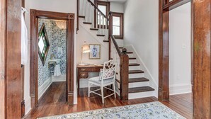 A wooden staircase with a chandelier, a desk with a chair, and patterned wallpaper. - Home in East End Historic Galveston, Coco Shores (Galveston)
