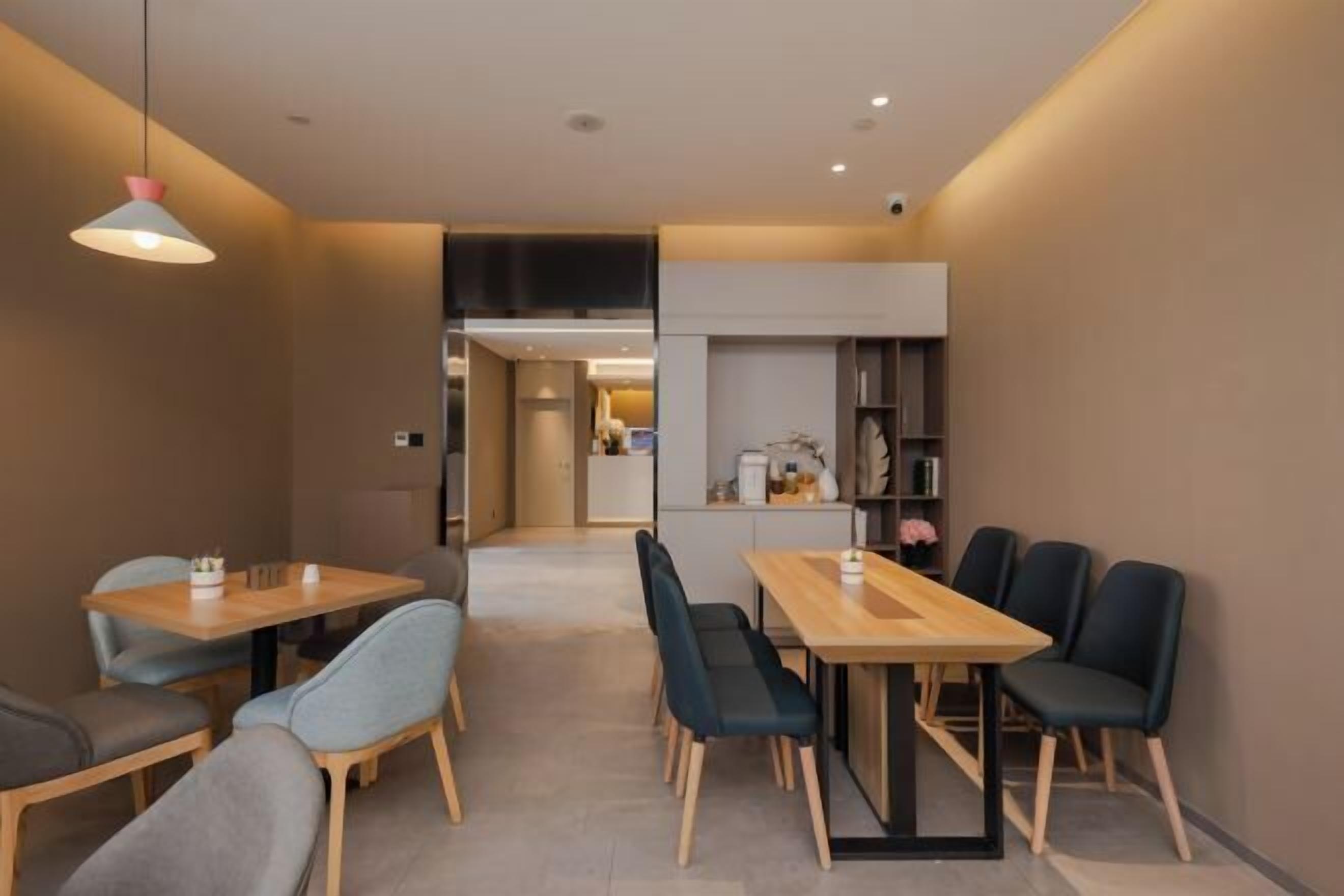 A modern dining area with two wooden tables and chairs, a pendant light, and a view into a kitchen area.