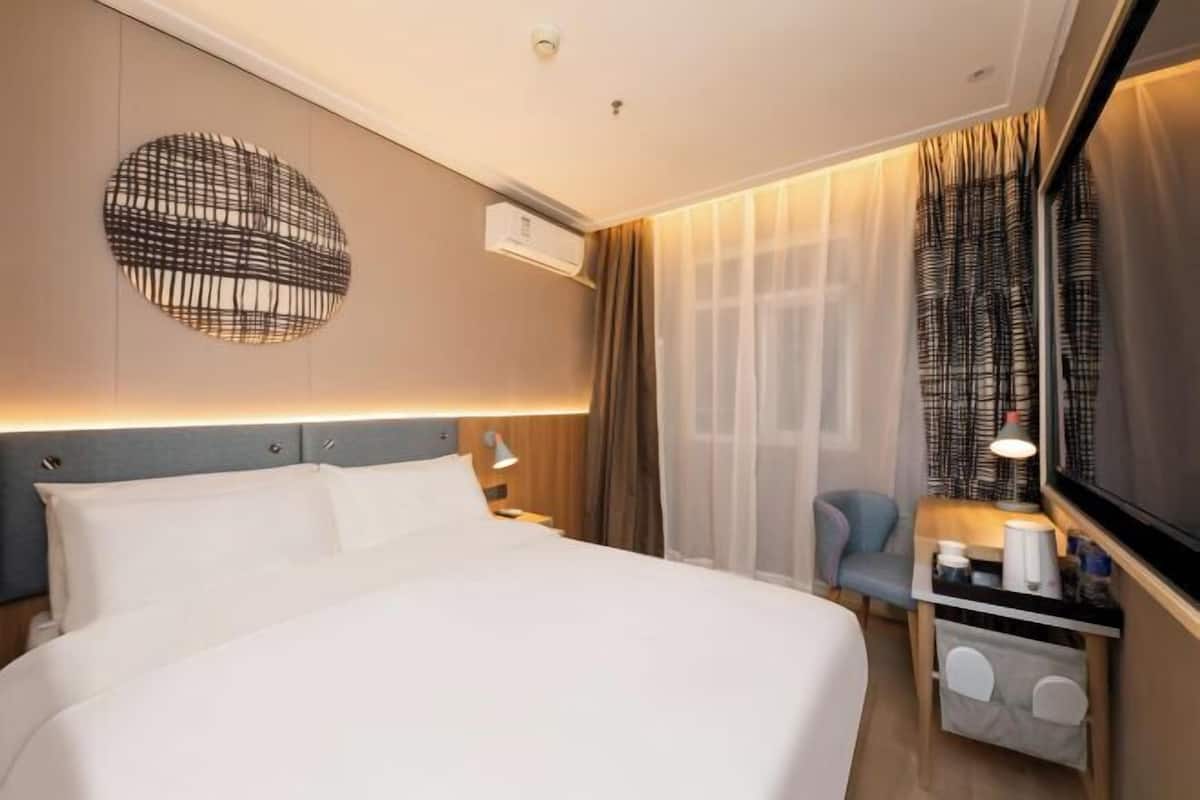 A hotel room with a bed, bedside table, lamp, and curtains.