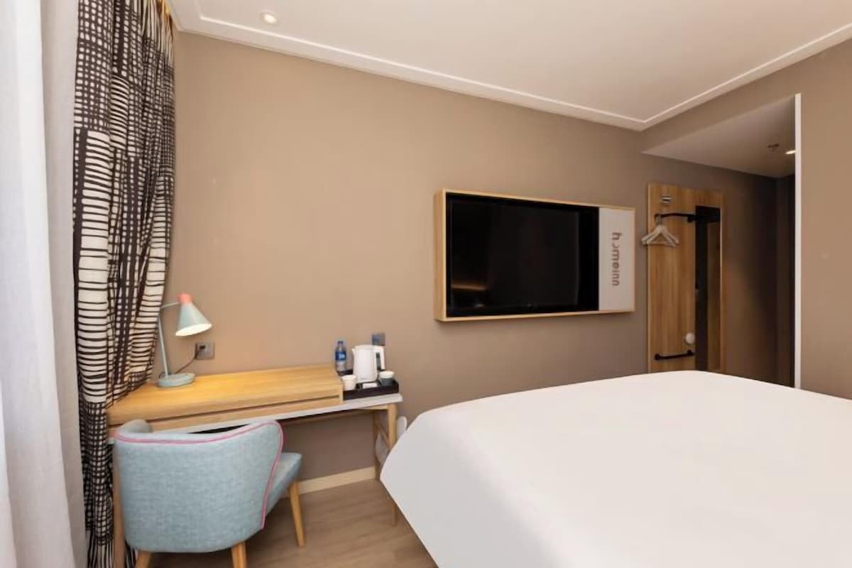A hotel room with a bed, a desk with a chair, a TV, and a wardrobe.