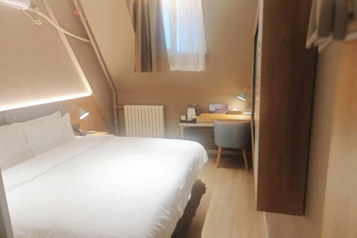 A hotel room with a bed, a desk, a chair, and a radiator.