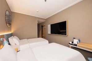 Quarto de hotel com duas camas, uma televisão de tela plana, uma mesa de cabeceira com abajur e uma obra de arte na parede.