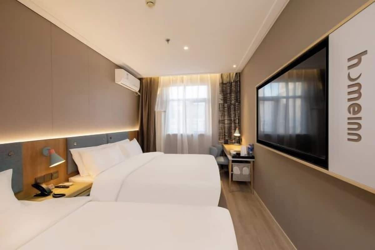 A hotel room with two beds, a desk, a TV, and a large window with curtains.