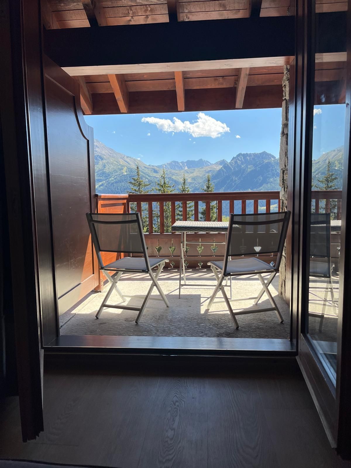 A balcony with a table and chairs, overlooking a mountainous landscape.
