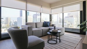 A modern living room with a sectional sofa, a round coffee table, and large windows offering a city view. - Liven in Miraflores by Wynwood House (Lima)