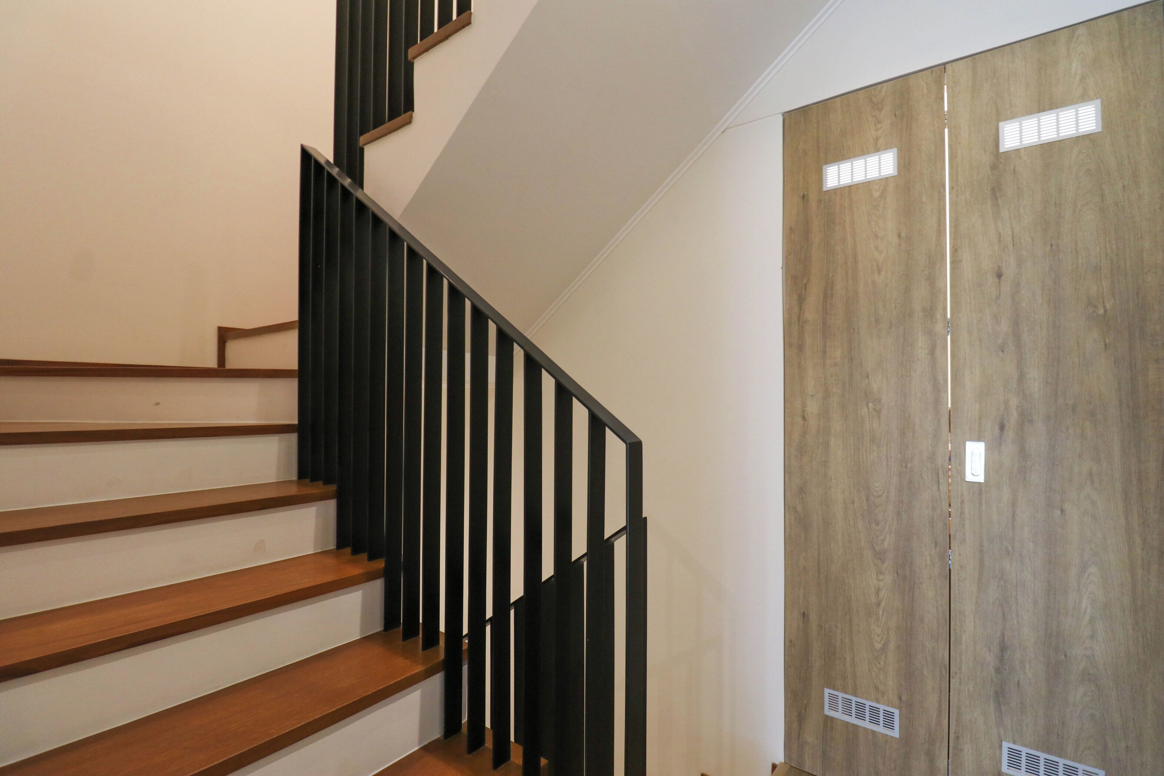 A staircase with wooden steps and black railings, leading to a wooden door with ventilation slats.