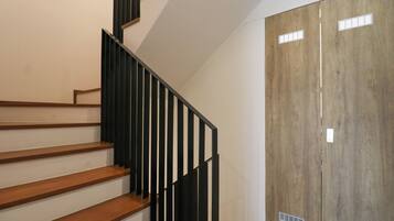 A staircase with wooden steps and black railings, leading to a wooden door with ventilation slats.