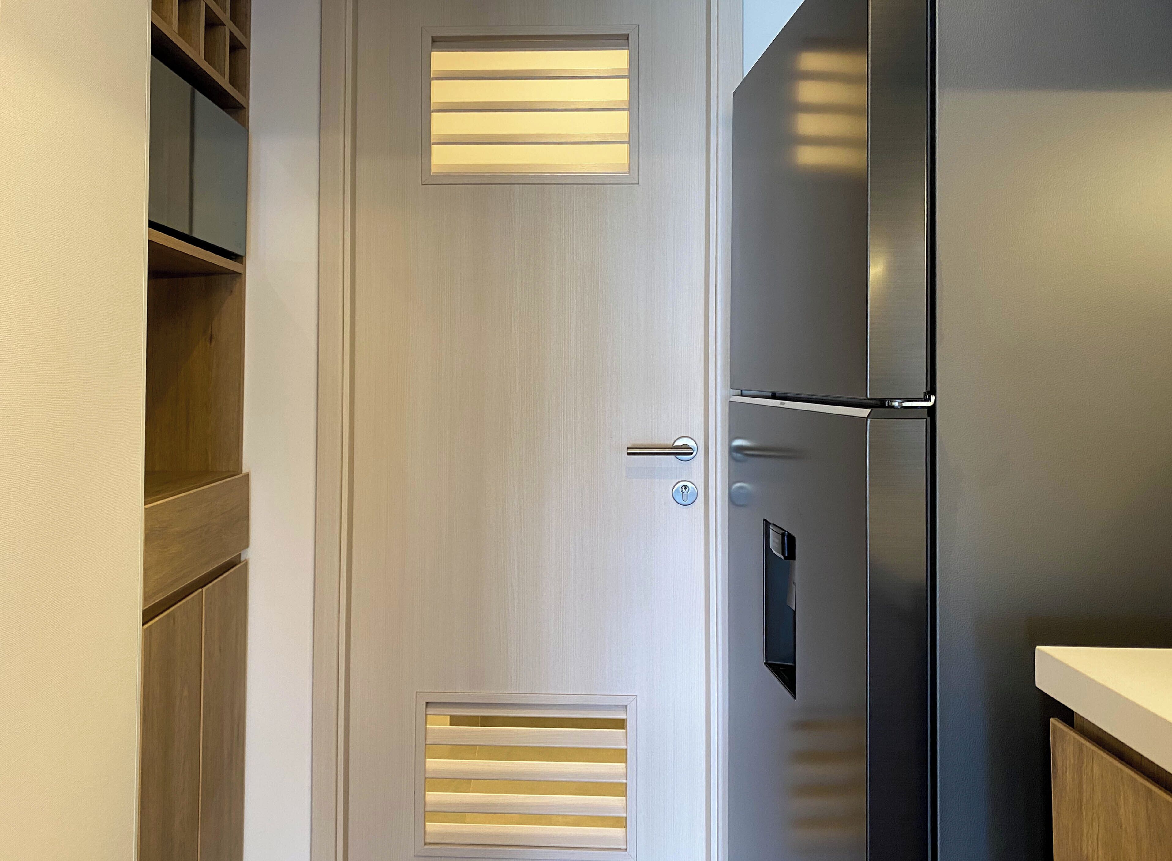 Una cocina moderna con refrigerador de acero inoxidable, armarios de madera y una puerta con paneles de ventilación.