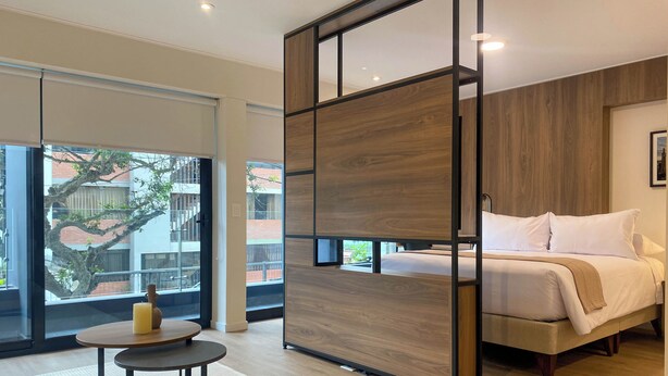A modern bedroom with a large bed, a wooden partition, and a view of the outside. - Liven in Miraflores by Wynwood House (Lima)
