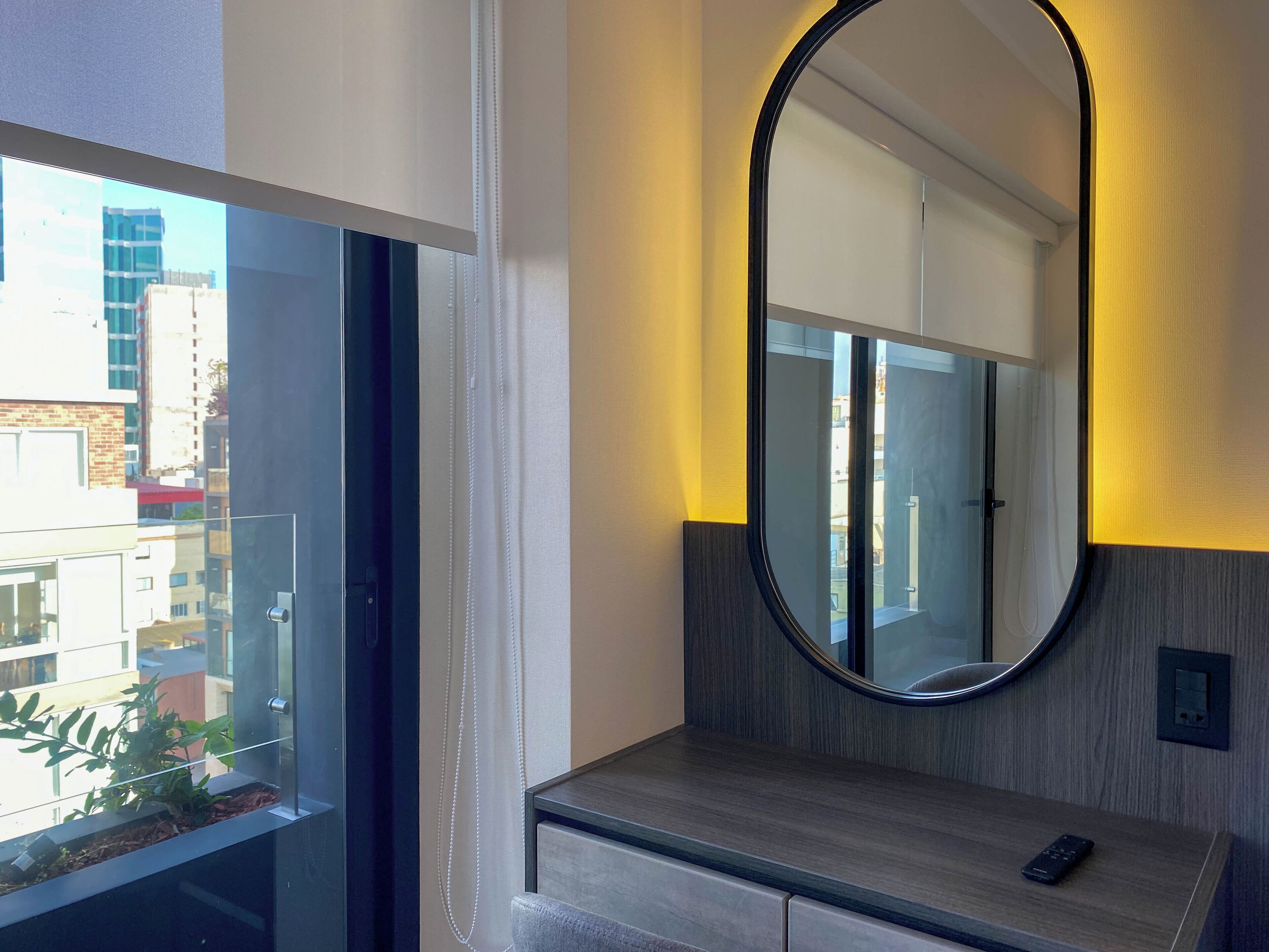 A modern bathroom with a large mirror, wooden vanity, and a view of the city through the window.