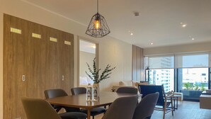 A modern dining area with a wooden table and chairs, a hanging light fixture, and a view of the city through large windows. - Liven in Miraflores by Wynwood House (Lima)