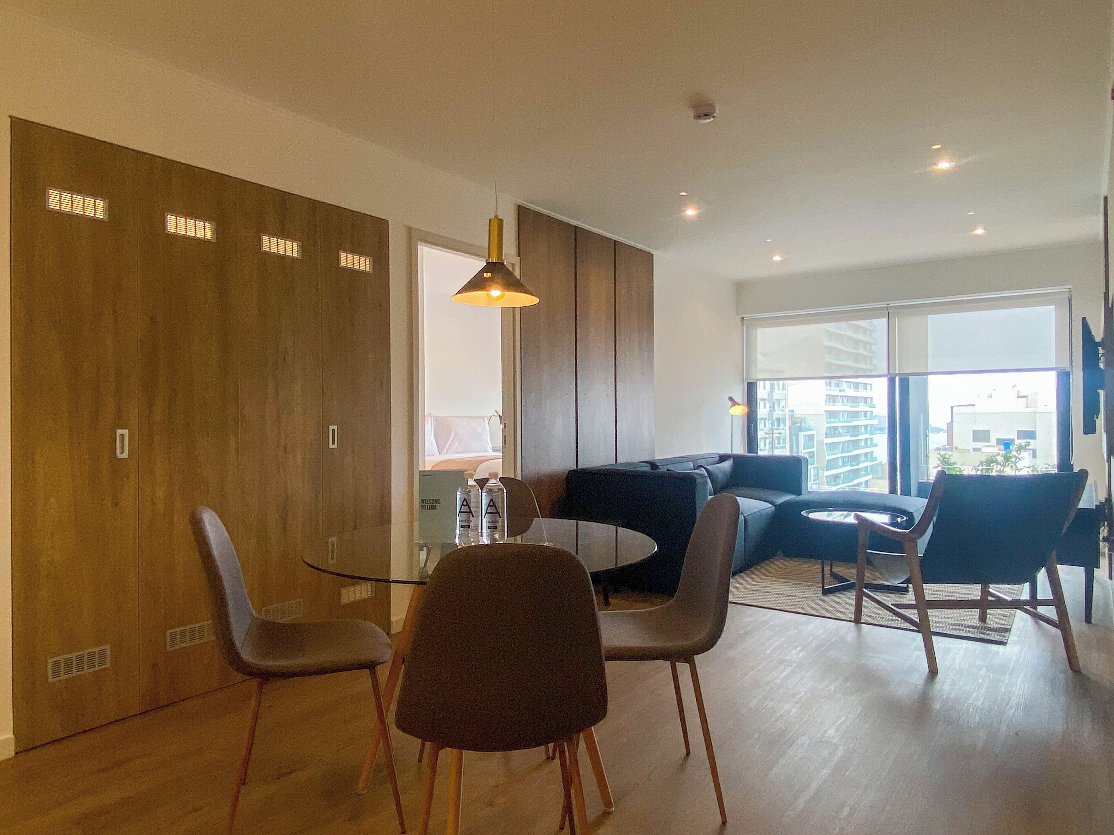A modern dining area with a glass table, four chairs, and a sofa.