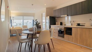 A modern kitchen with wooden cabinets, a dining area with a table and chairs, and a view of the city through large windows. - Liven in Miraflores by Wynwood House (Lima)