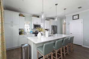 A modern kitchen with white cabinets, stainless steel appliances, and a central island with bar stools. - Cozy & Bright Townhome w/EV Charger-Walk to Beach (Perdido Key)