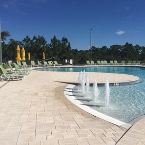 A swimming pool with a fountain, sun loungers, and umbrellas.
