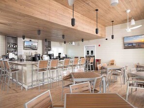 A modern restaurant with a bar area, multiple seating options including tables and chairs, and a wooden ceiling.