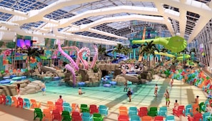 Un parc aquatique intérieur avec des toboggans, une piscine et des chaises colorées.
