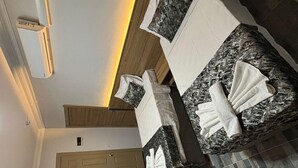 A modern hotel room with a wooden ceiling, a black marble-topped bed, a wooden cabinet, and a small table with towels. - Akapella (Denizli)