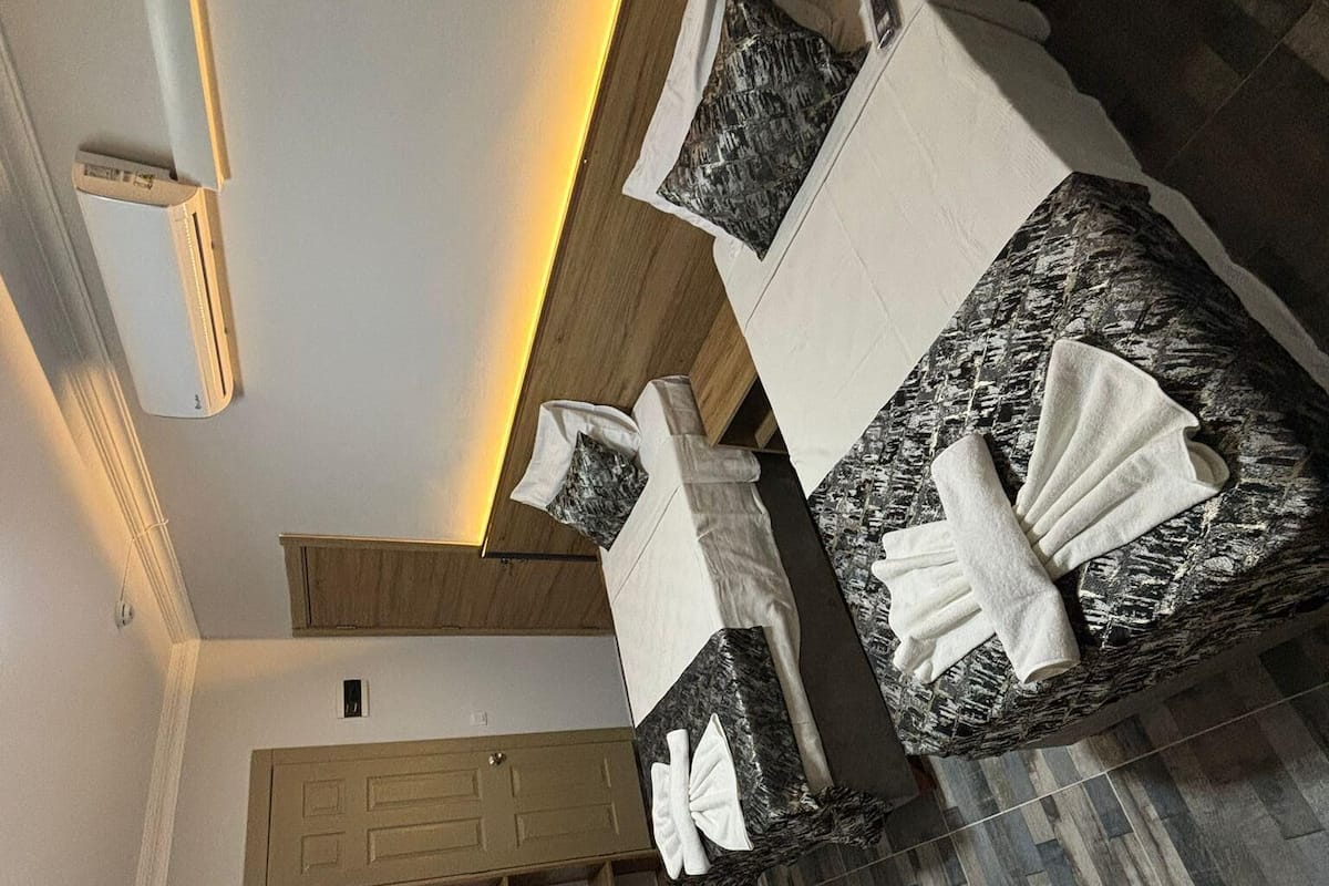 A modern hotel room with a wooden ceiling, a black marble-topped bed, a wooden cabinet, and a small table with towels.