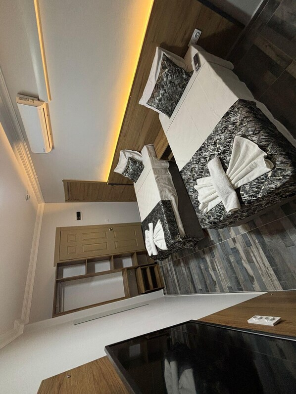 Une chambre d’hôtel moderne avec un plafond en bois, un lit surmonté d’un plateau en marbre noir, une armoire en bois et une petite table avec des serviettes.