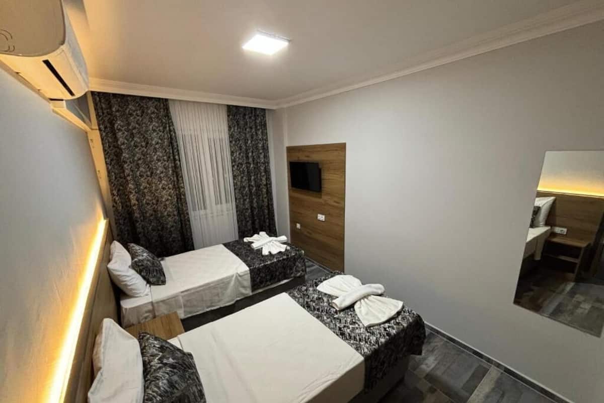 A hotel room with two beds, a flat-screen TV mounted on the wall, a mirror, and a ceiling light.