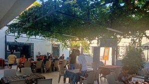 An outdoor cafe with tables and chairs, covered by a pergola with vines. - Akapella (Denizli)