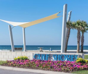 A sign with 'Culfs Shore' written in blue letters, a white canopy structure, and a row of pink flowers. - Stunning Luxury Home- WALK to POOL & BEACH! (Gulf Shores)