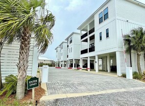 A gated entrance to a residential building with a paved driveway and a palm tree. - Stunning Luxury Home- WALK to POOL & BEACH! (Gulf Shores)