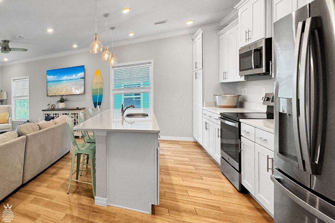 A modern kitchen with white cabinetry, stainless steel appliances, and a central island with bar stools.