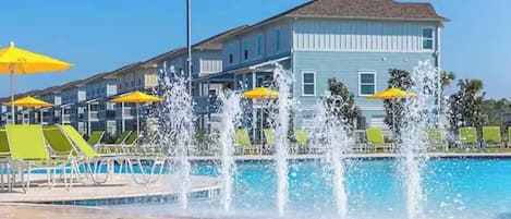 A swimming pool with water jets, surrounded by lounge chairs and yellow umbrellas.