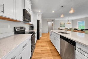 Une cuisine moderne avec des meubles blancs, des appareils en acier inoxydable et un plancher en bois.