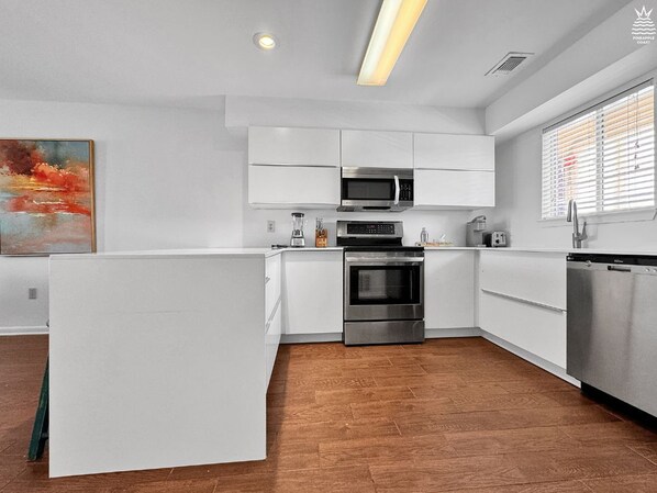 A modern kitchen with white cabinetry, stainless steel appliances, and a herringbone wood floor. - Sunset Harbor Condo w/Balcony, Fishing Pier & Pool (Navarre)