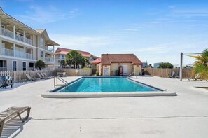 A swimming pool with lounge chairs and a small building, surrounded by a wooden fence and palm trees. - Sunset Harbor Condo w/Balcony, Fishing Pier & Pool (Navarre)