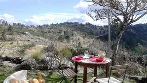Un espacio de comedor al aire libre con una mesa y sillas, rodeado por un paisaje natural con colinas y árboles.