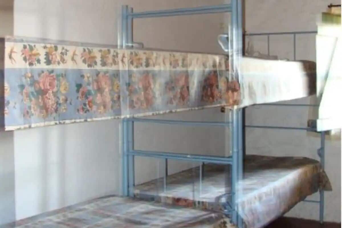 A bunk bed with floral-patterned bedding in a room with wooden ceiling beams and plain walls.