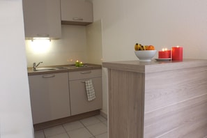A kitchen with a sink, cabinets, and a countertop. There are candles and a bowl of fruit on the counter. - Vvf Villages Sigean (Sigean)