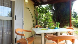 A covered patio with a table and chairs, a door, and greenery in the background. - Vvf Villages Sigean (Sigean)