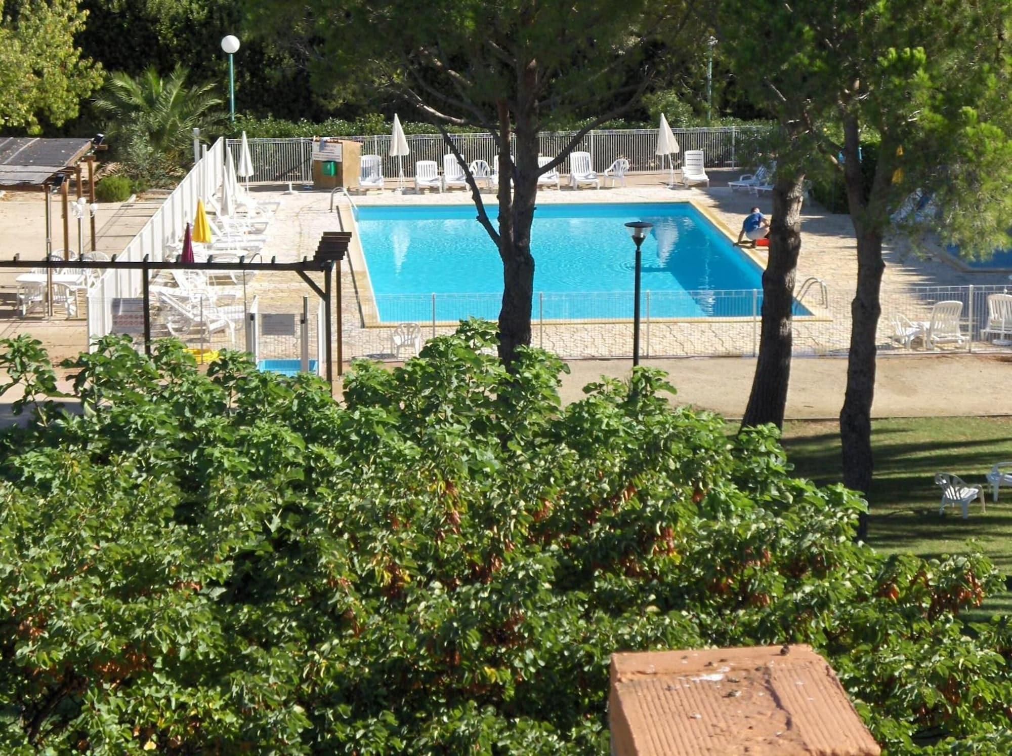 Une piscine à l’eau d’un bleu cristallin, entourée de chaises longues blanches et d’un espace abrité agrémenté d’une pergola.