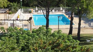 A swimming pool with a clear blue water, surrounded by white lounge chairs and a covered area with a pergola. - Vvf Villages Sigean (Sigean)