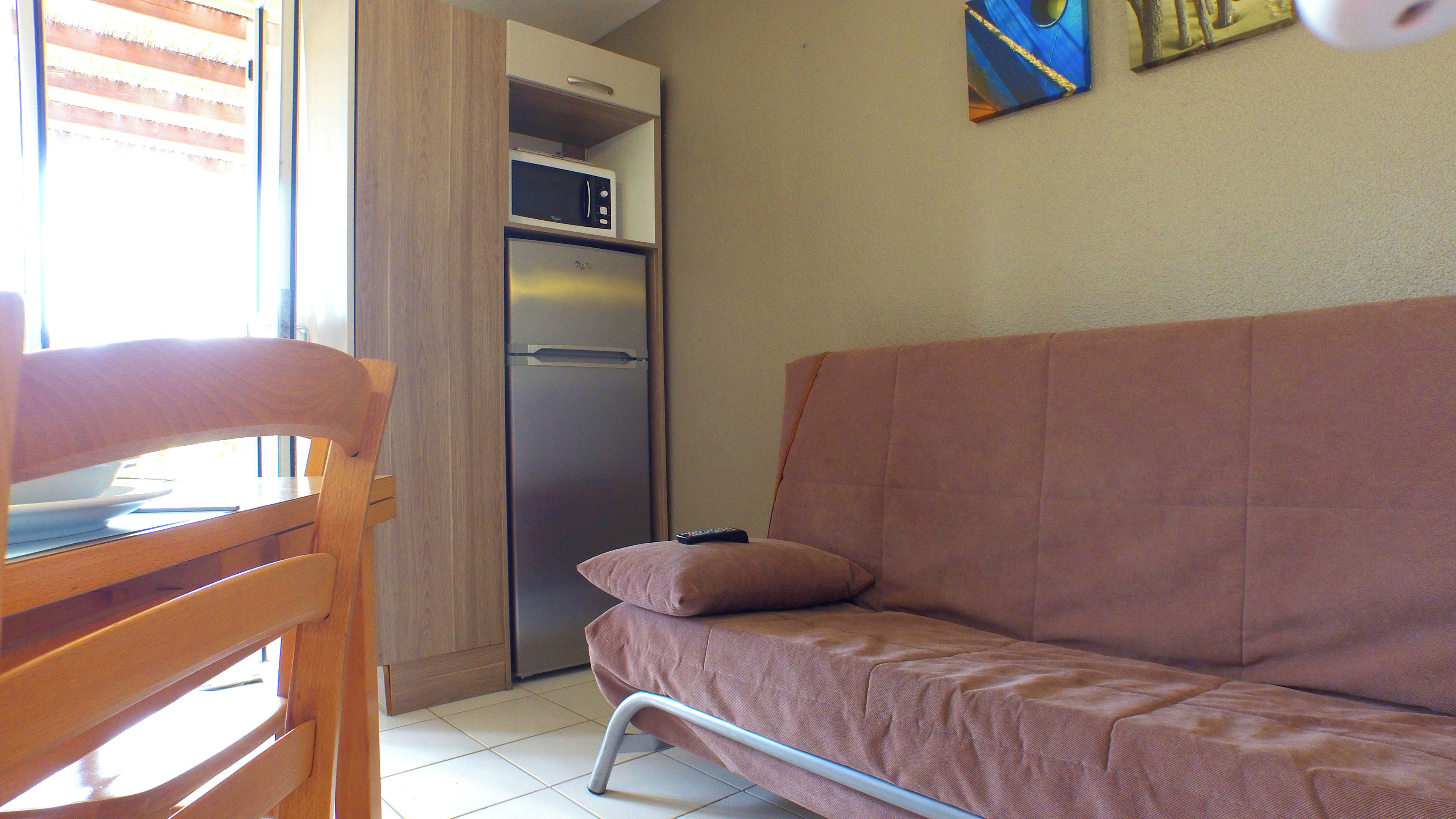 Une petite cuisine équipée d’un réfrigérateur et d’un four à micro-ondes, une table à manger en bois avec des chaises, et un canapé rose.