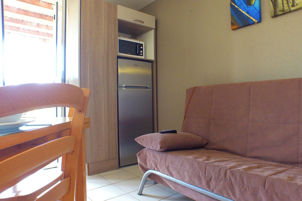 A kitchenette with a refrigerator and microwave, a wooden dining table with chairs, and a pink sofa.