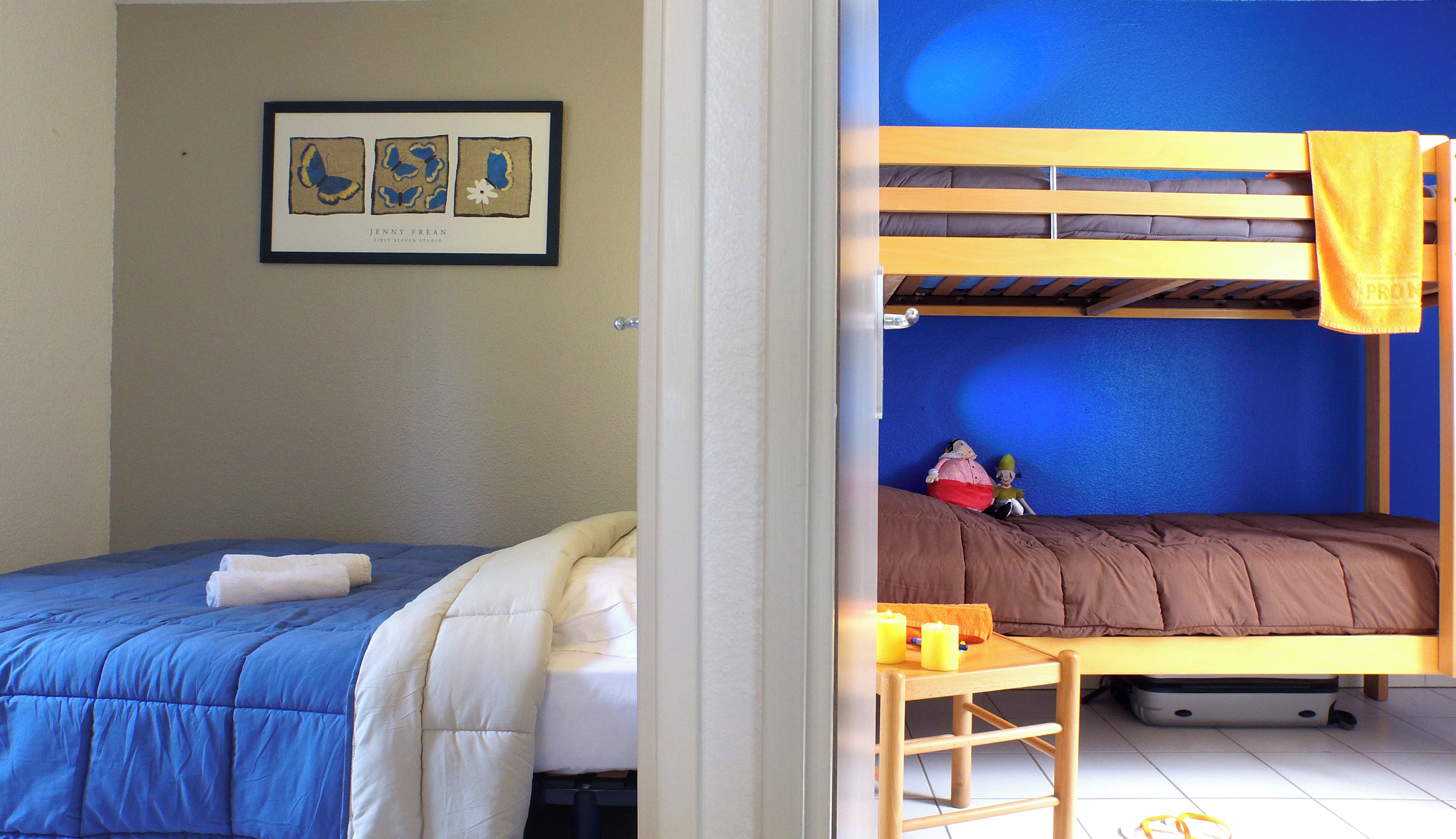 Une chambre avec deux lits, l’un recouvert d’une couverture bleue et l’autre d’une couverture marron. Un tableau encadré est accroché au mur, au-dessus du lit bleu.