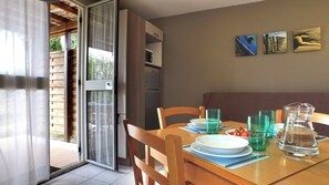 Un comedor con una mesa preparada para dos, un puerta corrediza de vidrio que da a un espacio exterior y un refrigerador al fondo.