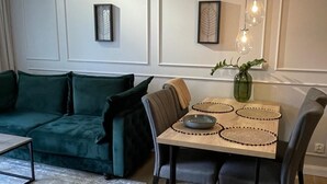 A modern living room with a green sofa, a dining table with placemats, and pendant lighting. - Apartamenty na Wydmach BR (Międzywodzie)