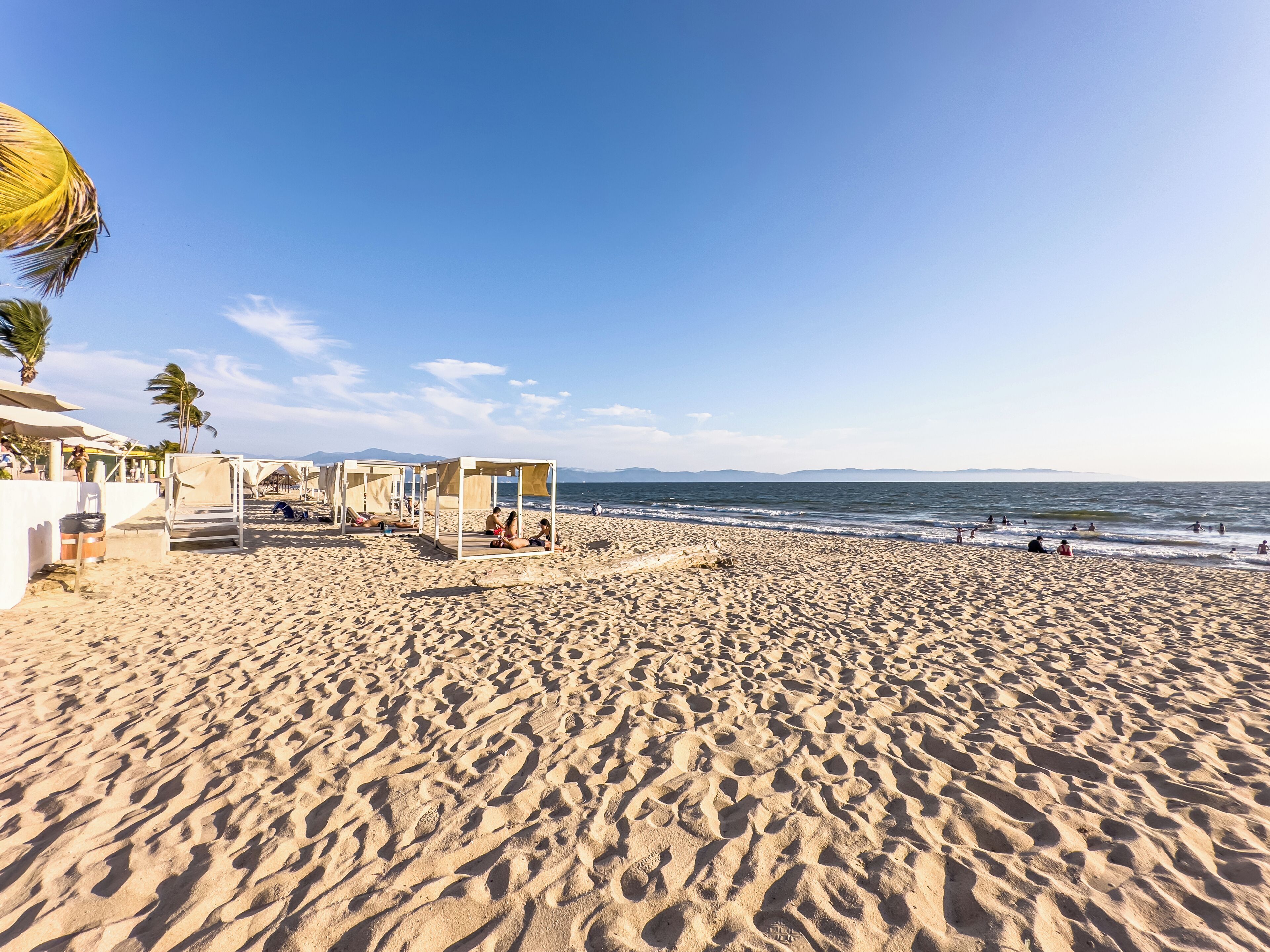 A beach with sand, a few people, and a clear sky.