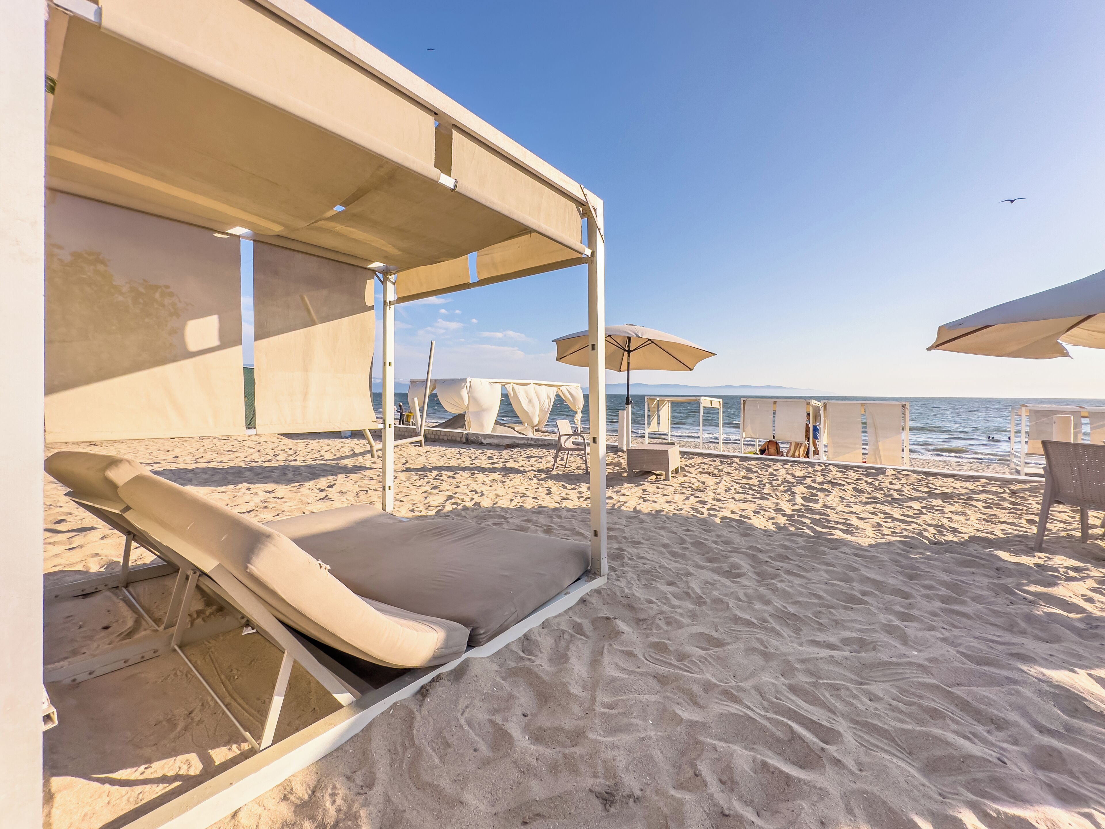 Ein Strand mit Liegestühlen und Sonnenschirmen, ein klarer Himmel und das Meer im Hintergrund.