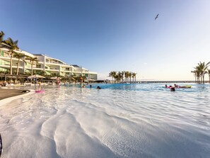 A resort pool area with a large pool, palm trees, and a building with multiple balconies. - ARIA Residence Beachfront luxury (Nuevo Nayarit)