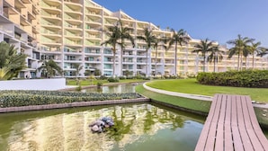 Un hotel moderno con varios pisos, un jardín ajardinado, un estanque con rocas y una terraza de madera.